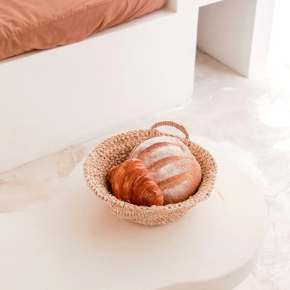 Woven basket with bread and croissant on a white surface