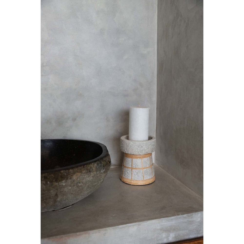 Ceramic candle holder with a white candle on a concrete surface against a gray wall.