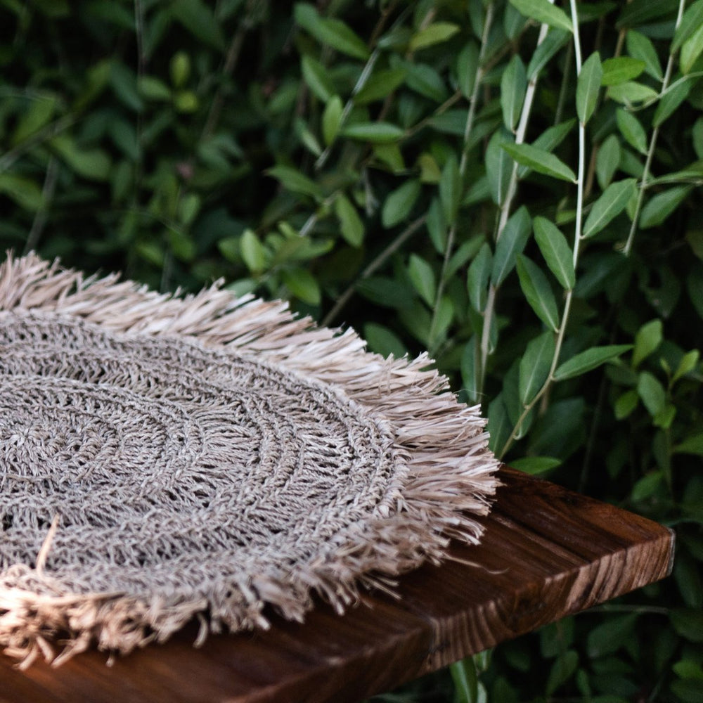 Textured woven mat on a wooden surface with green foliage in the background