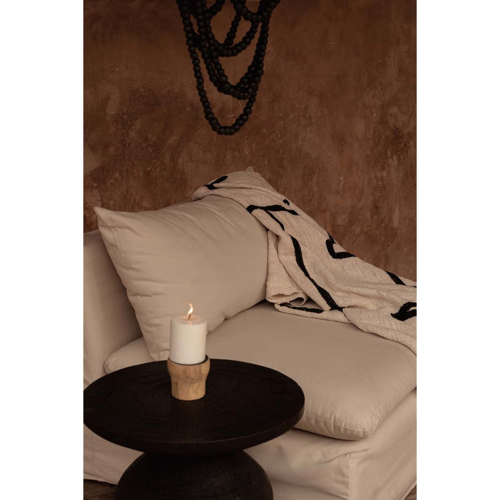 Beige sofa with a candle on a small round table against a brown wall.