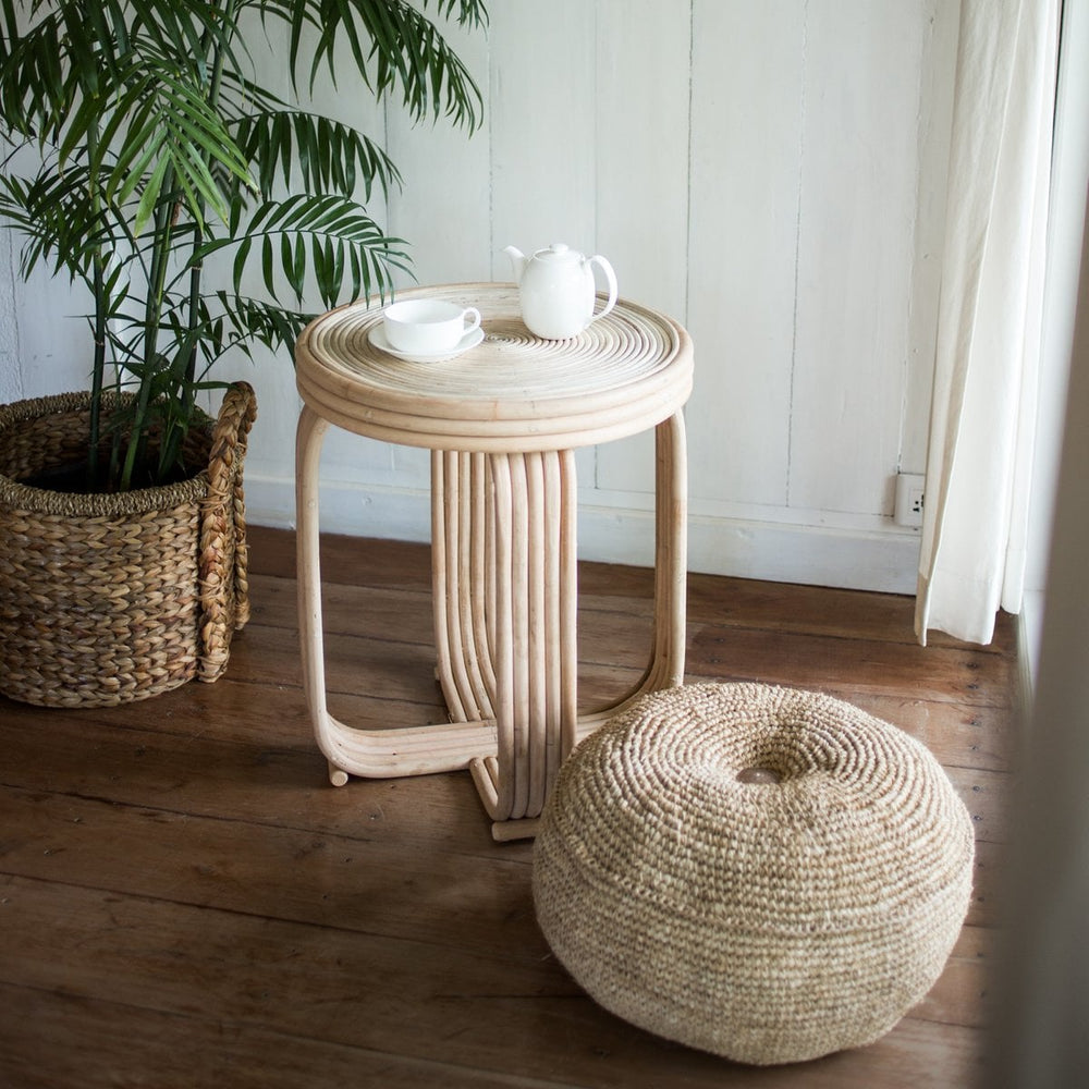Woven side table and ottoman with a plant in a room.