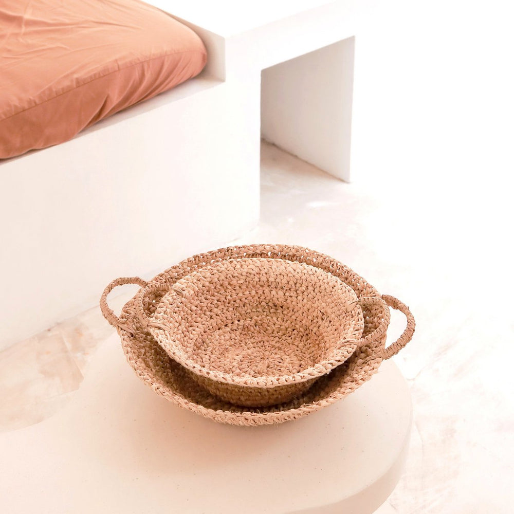 Set of woven baskets on a white surface with a pink cushion in the background