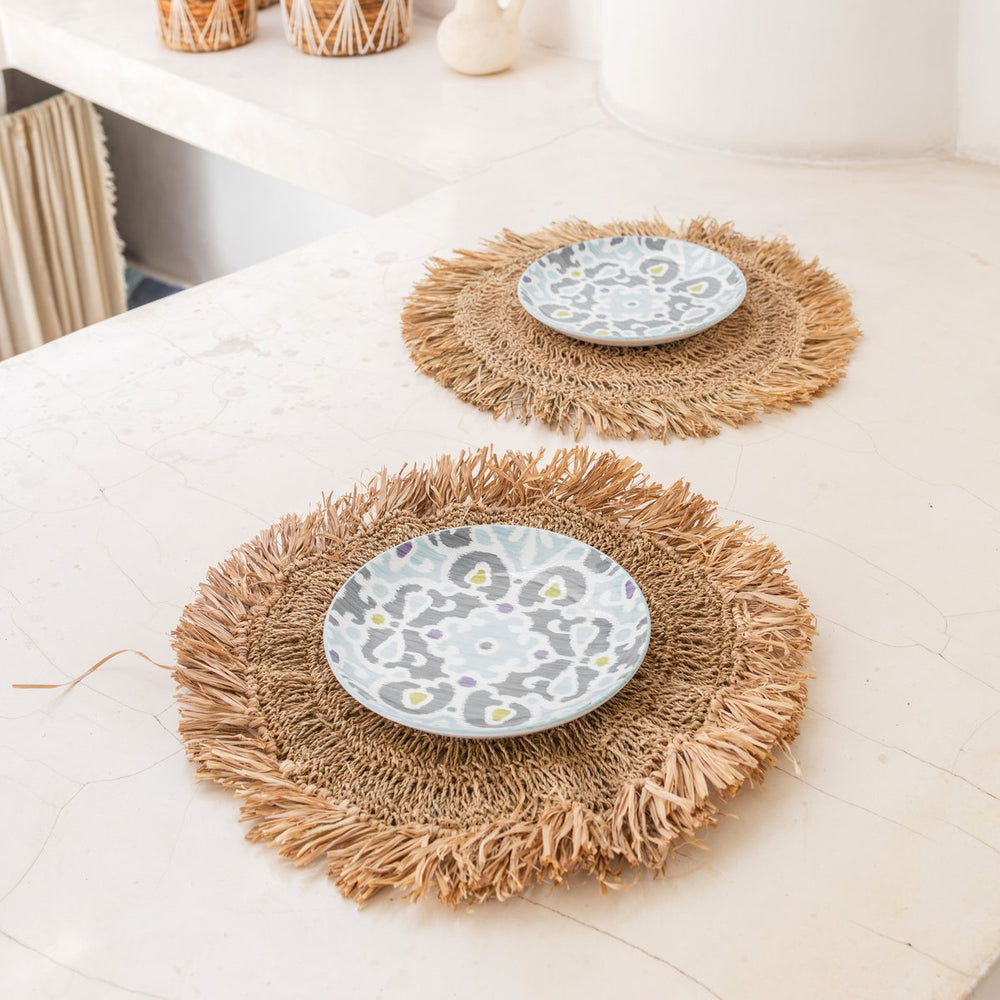 Two woven placemats with decorative plates on a light surface.