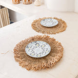 Two woven placemats with decorative plates on a light surface.