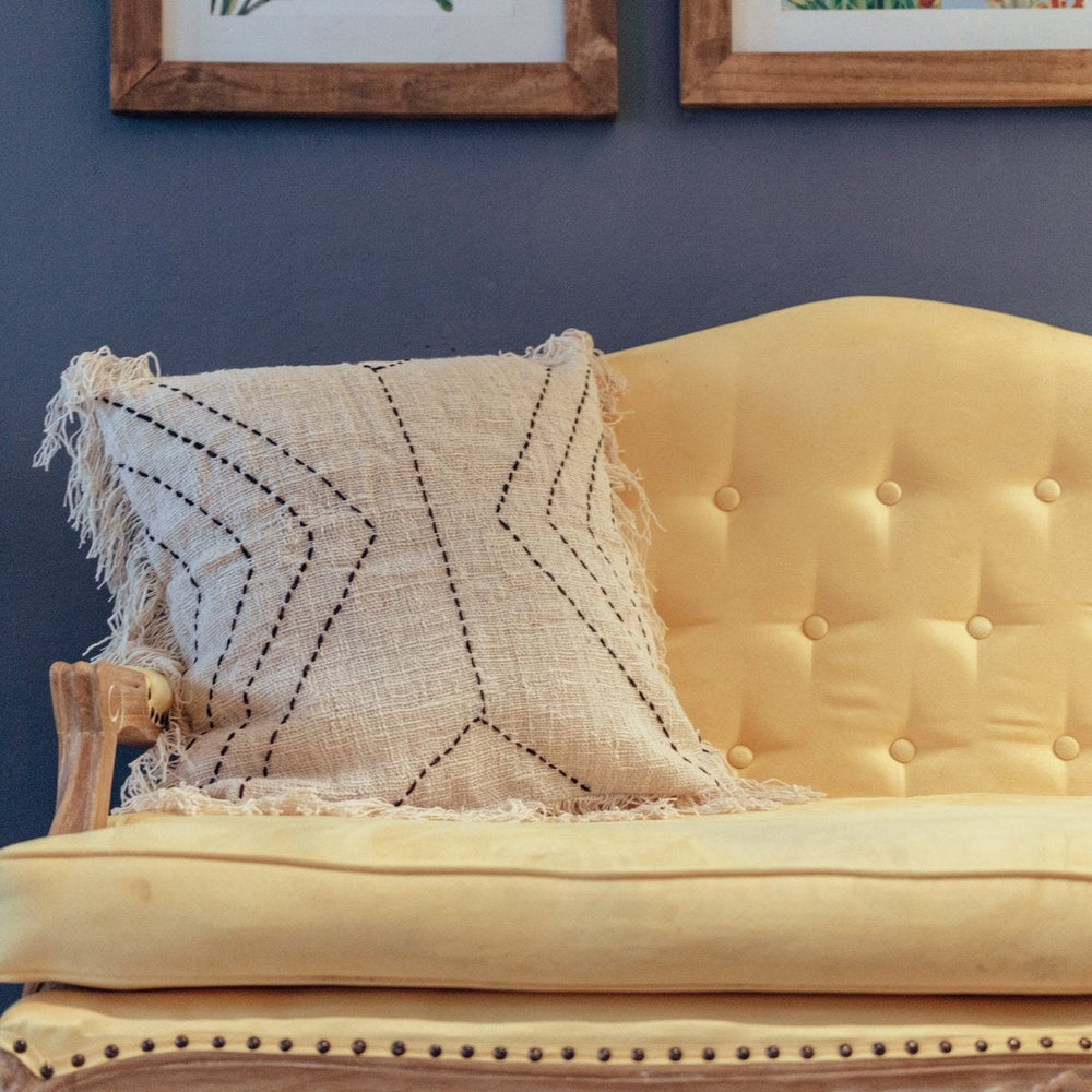 Yellow sofa with a textured pillow against a blue wall with framed pictures.