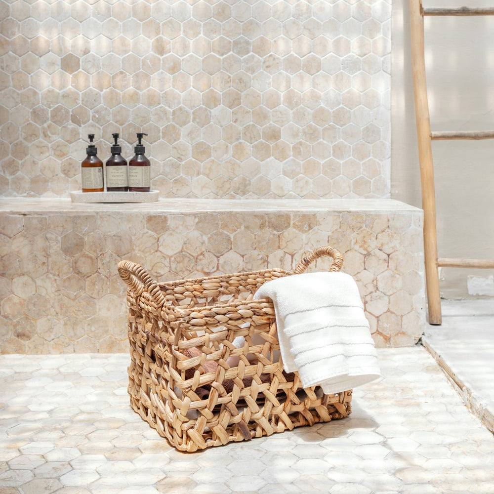 Wicker laundry basket with a white towel on a tiled bathroom floor.