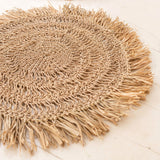 Round woven mat with fringes on a light wooden floor