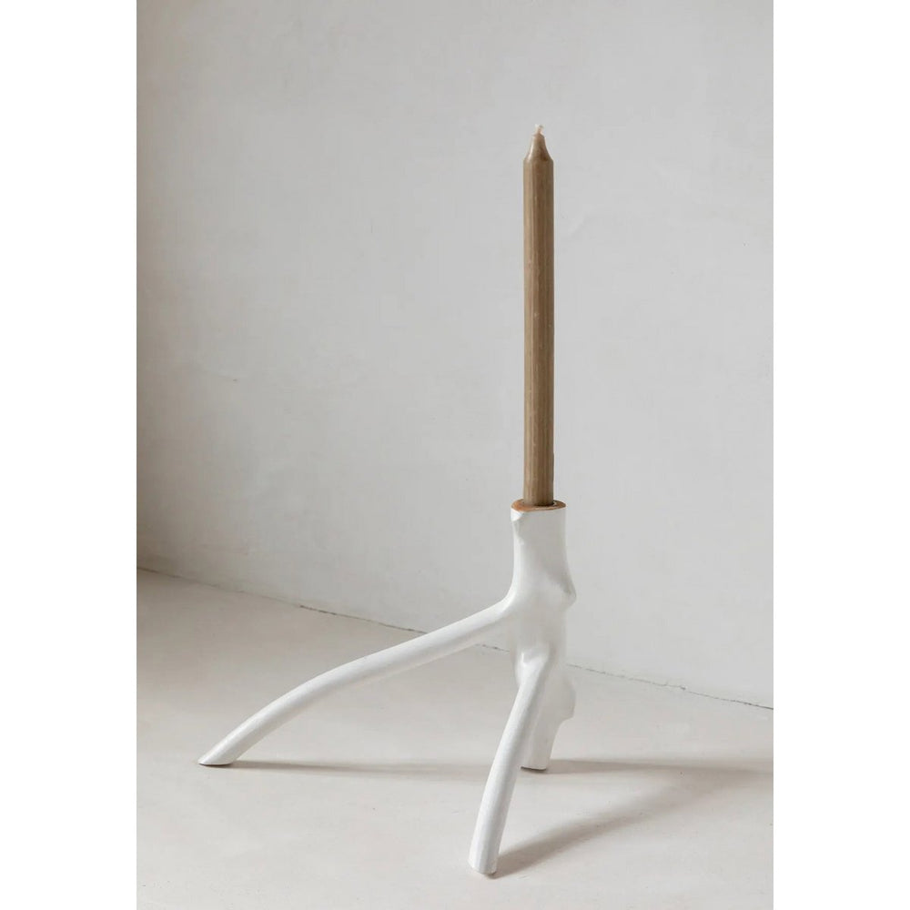 White candle holder with a beige candle on a light gray background