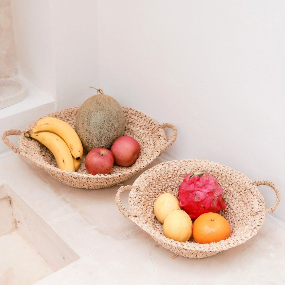 Two woven fruit bowls filled with various fruits on a light surface.