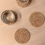 Round woven coasters on a wooden surface with glasses.