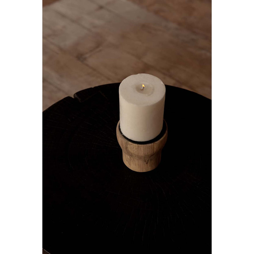 White candle in a wooden holder on a dark surface with a wooden floor background