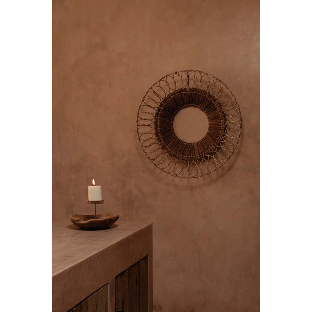 Decorative wall mirror with a candle on a wooden surface against a brown wall.