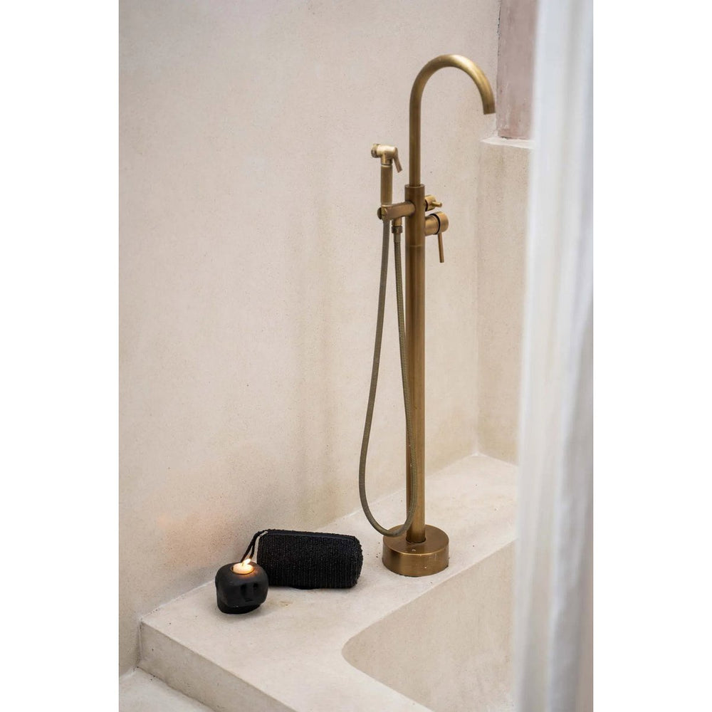 Brass freestanding bathtub faucet with handheld shower head in a bathroom setting.