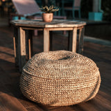 Round woven ottoman on a wooden floor with a blurred background