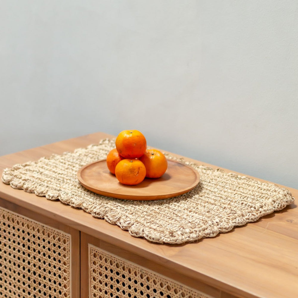 Oranges on a wooden plate on a textured woven placemat with a light gray background