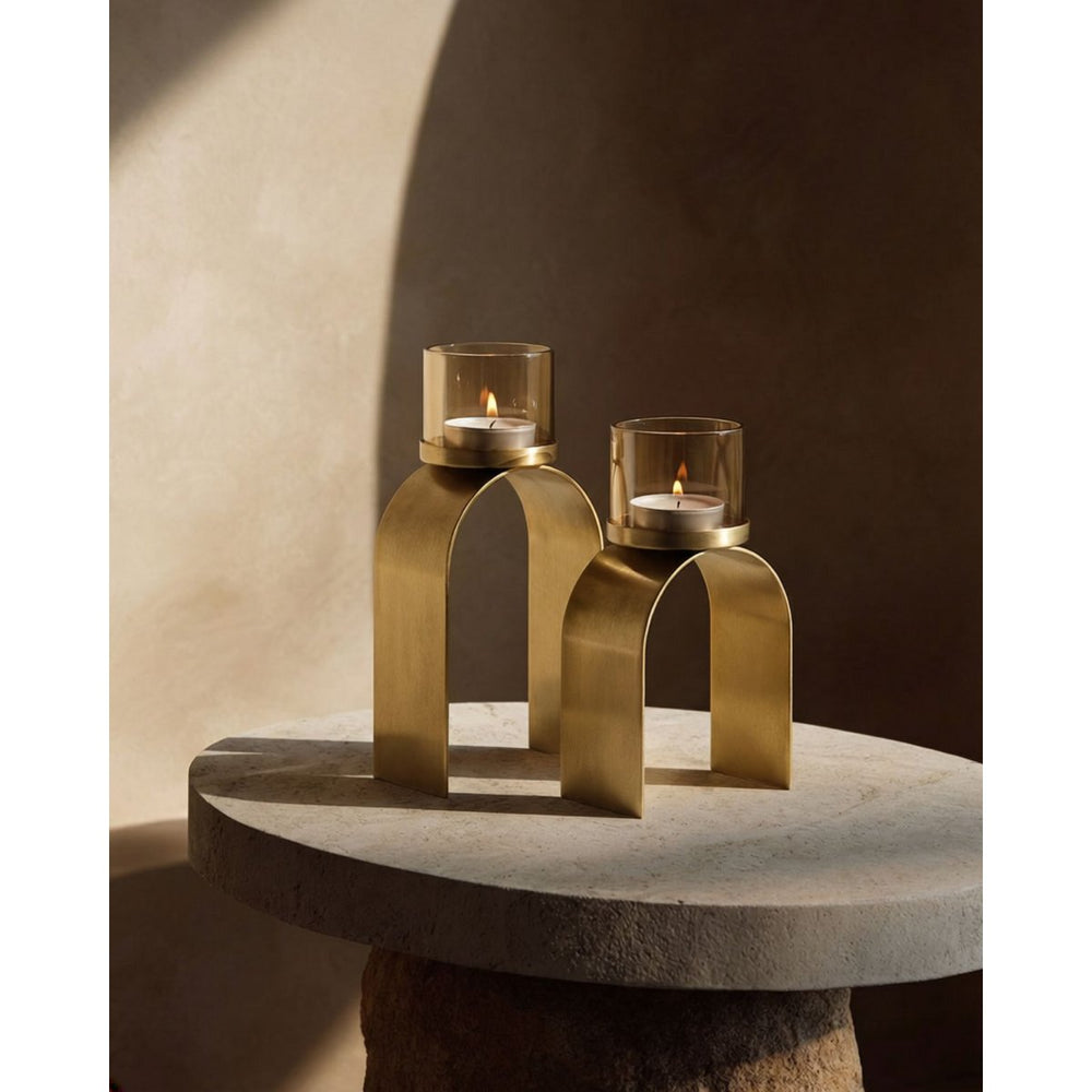 Two gold candle holders with candles on a stone surface against a neutral wall.