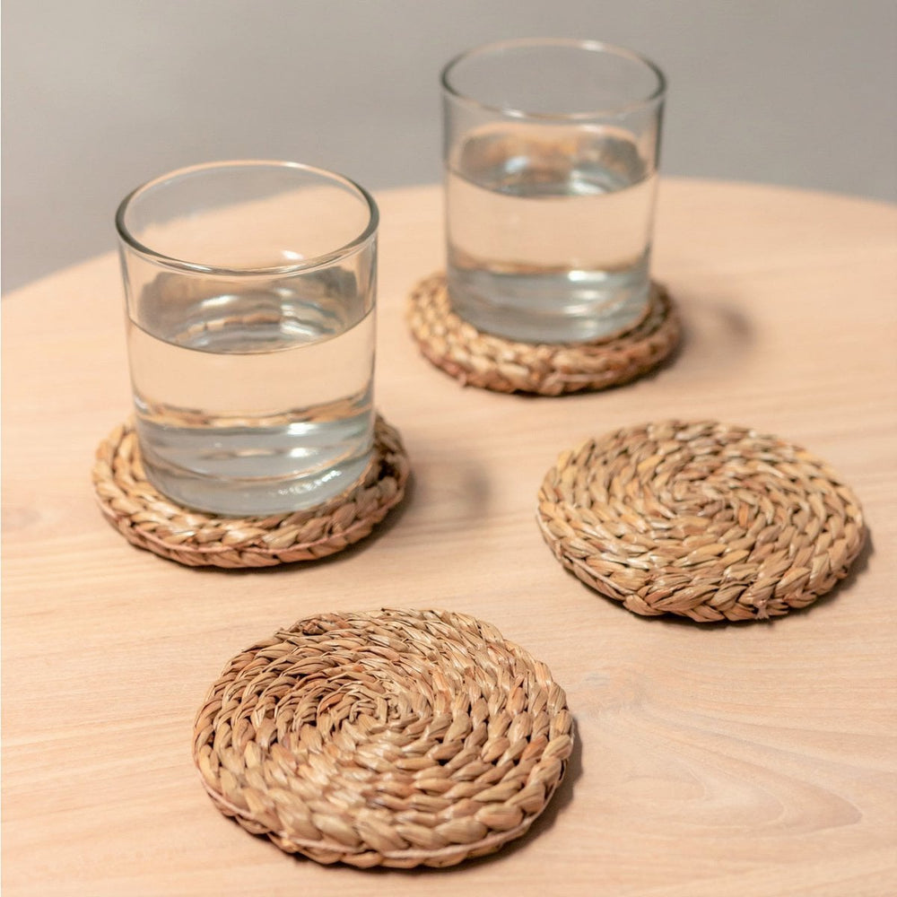 Two glasses of water on woven coasters on a wooden surface.