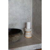 Ceramic candle holder with a white candle on a concrete surface against a gray wall.