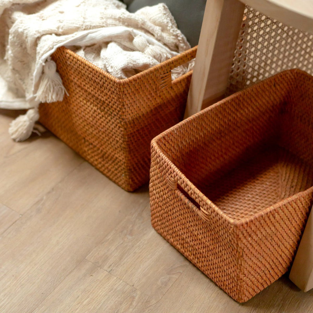 Two woven storage baskets on a wooden floor with a blanket partially visible.