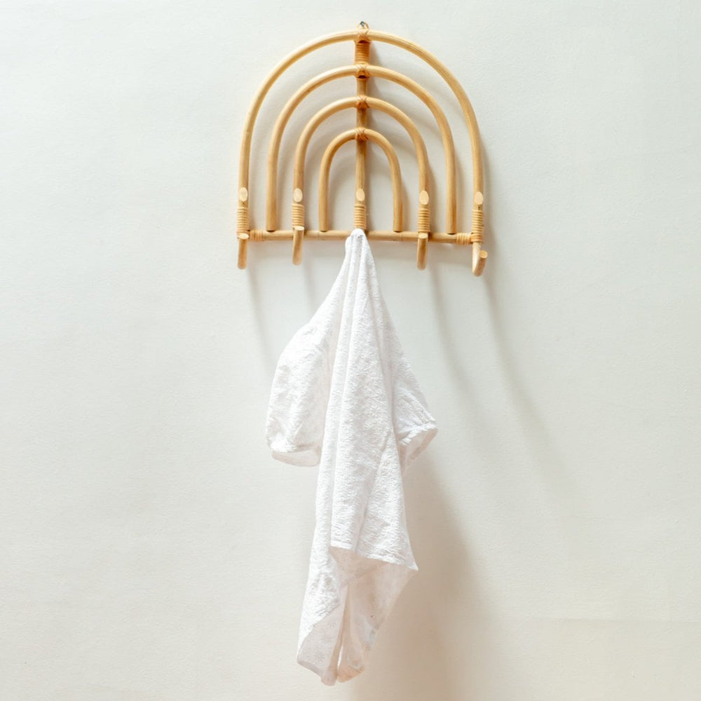 Wooden rainbow-shaped hook with a white towel on a plain wall