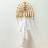 Wooden rainbow-shaped hook with a white towel on a plain wall