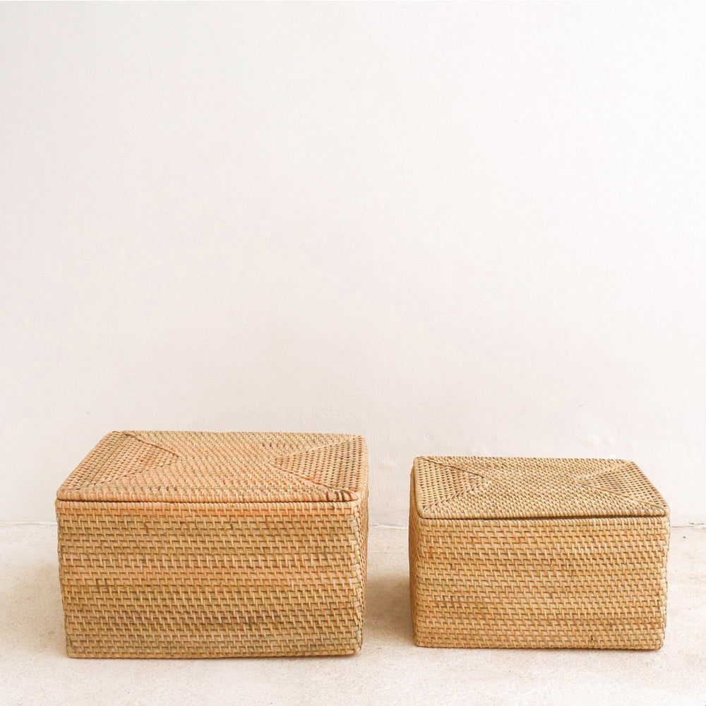 Two woven storage boxes on a light wooden floor with a white wall background