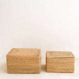 Two woven storage boxes on a light wooden floor with a white wall background