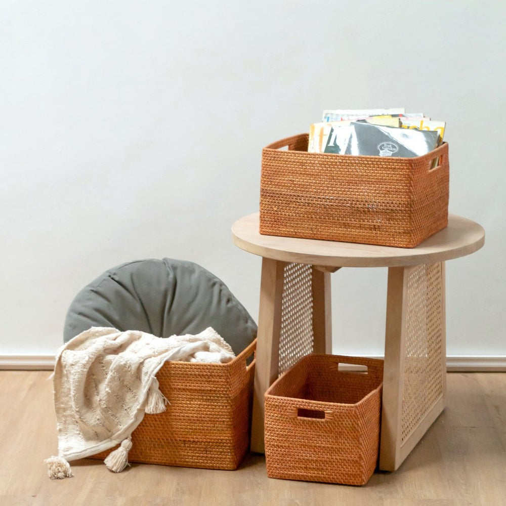Wicker baskets with a blanket and books on a wooden side table against a white wall.