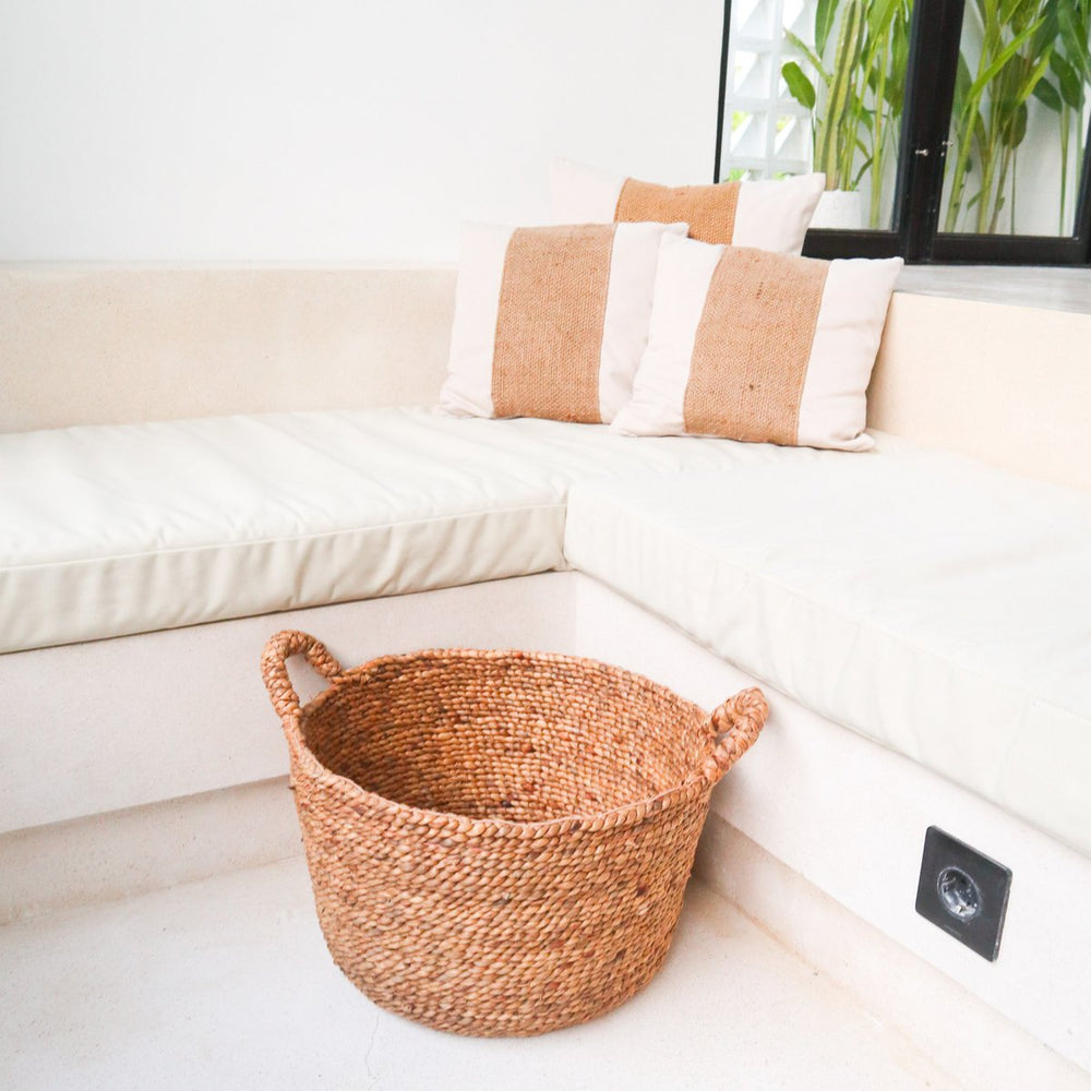 Woven basket on a white floor next to a beige sofa with pillows