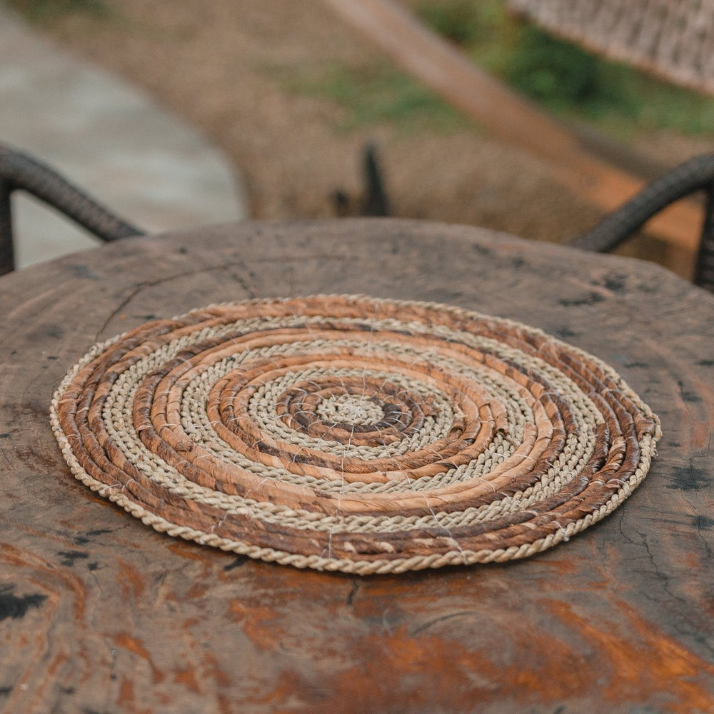Round woven placemat on a textured surface with blurred outdoor background