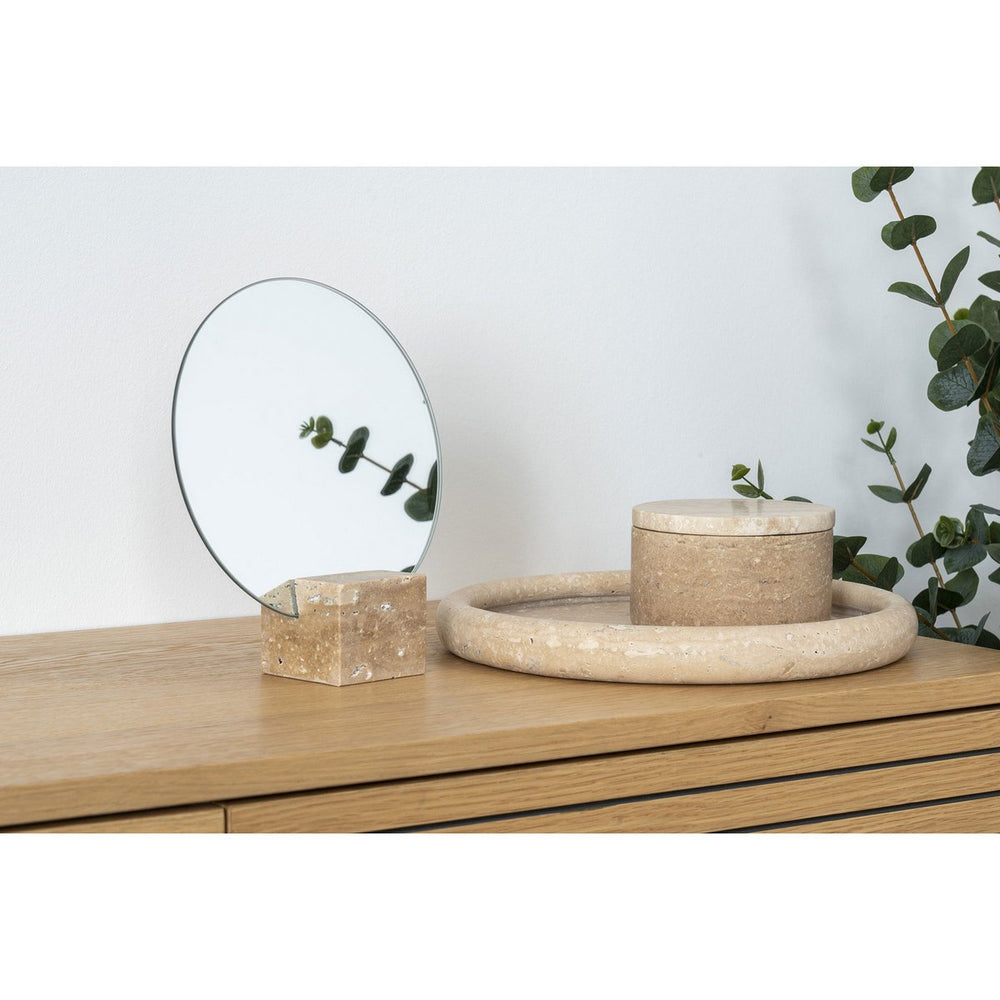 Decorative items including a round mirror, box, and bowl on a wooden surface with a plant in the background.