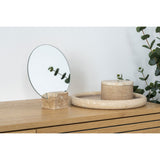 Decorative items including a round mirror, box, and bowl on a wooden surface with a plant in the background.