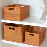 Three woven storage baskets on a white shelf with a white curtain in the background.