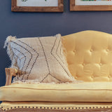 Yellow sofa with a textured pillow against a blue wall with framed pictures.