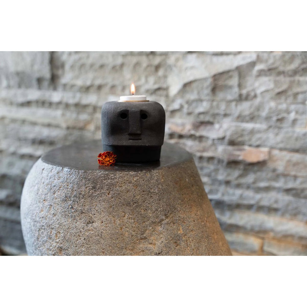 Ceramic candle holder shaped like a face with a lit candle on a stone surface.