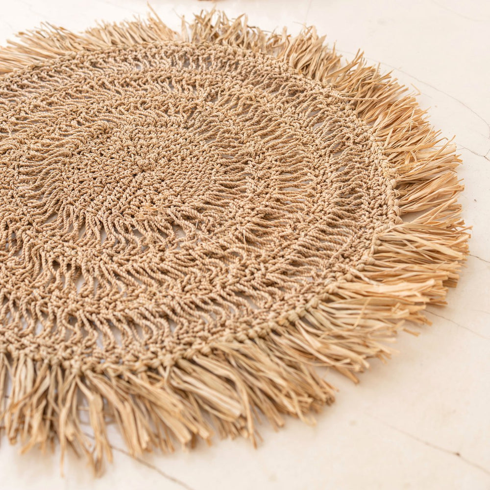 Round woven mat with fringes on a light wooden floor