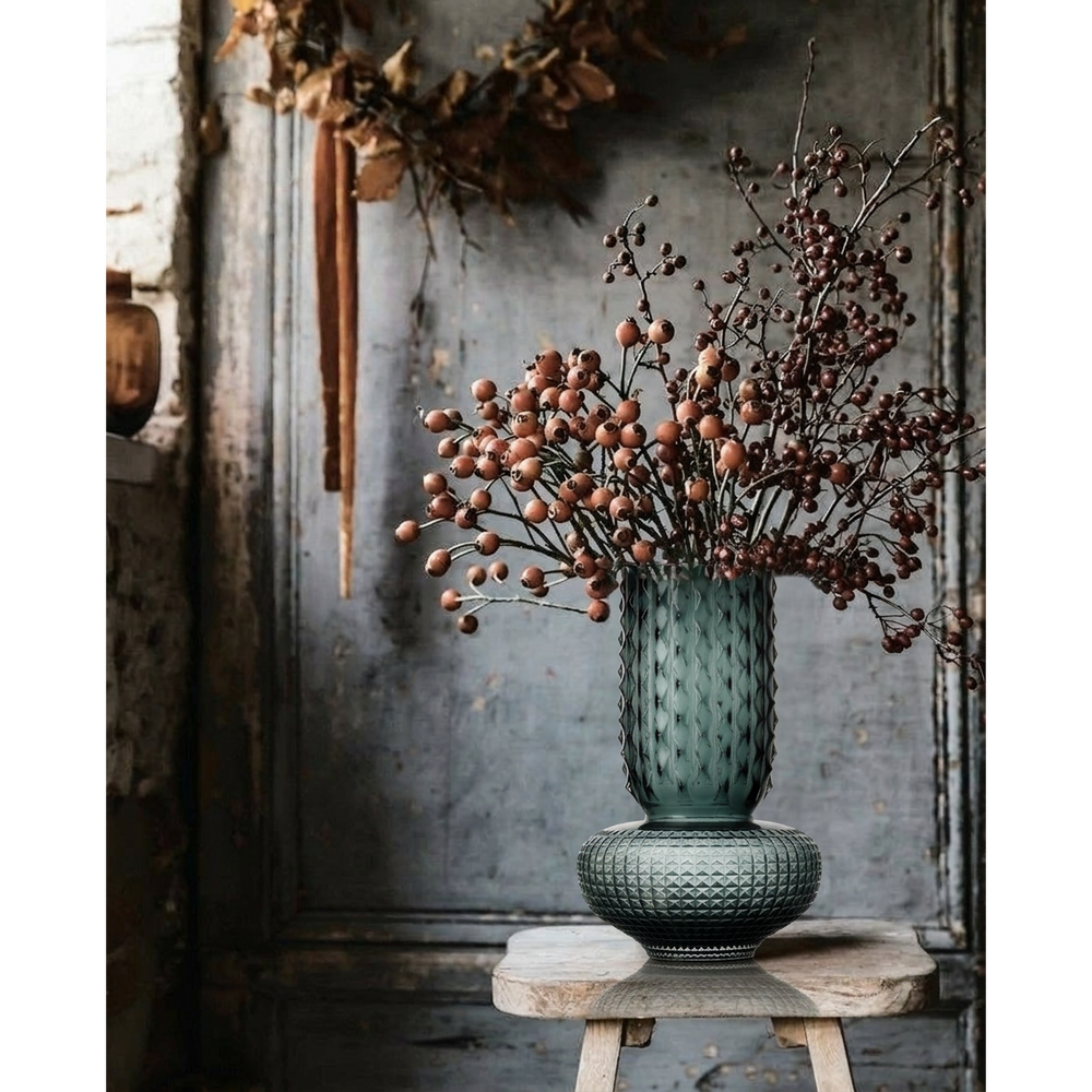 Decorative vase with dried flowers on a rustic wooden stool against a textured wall.