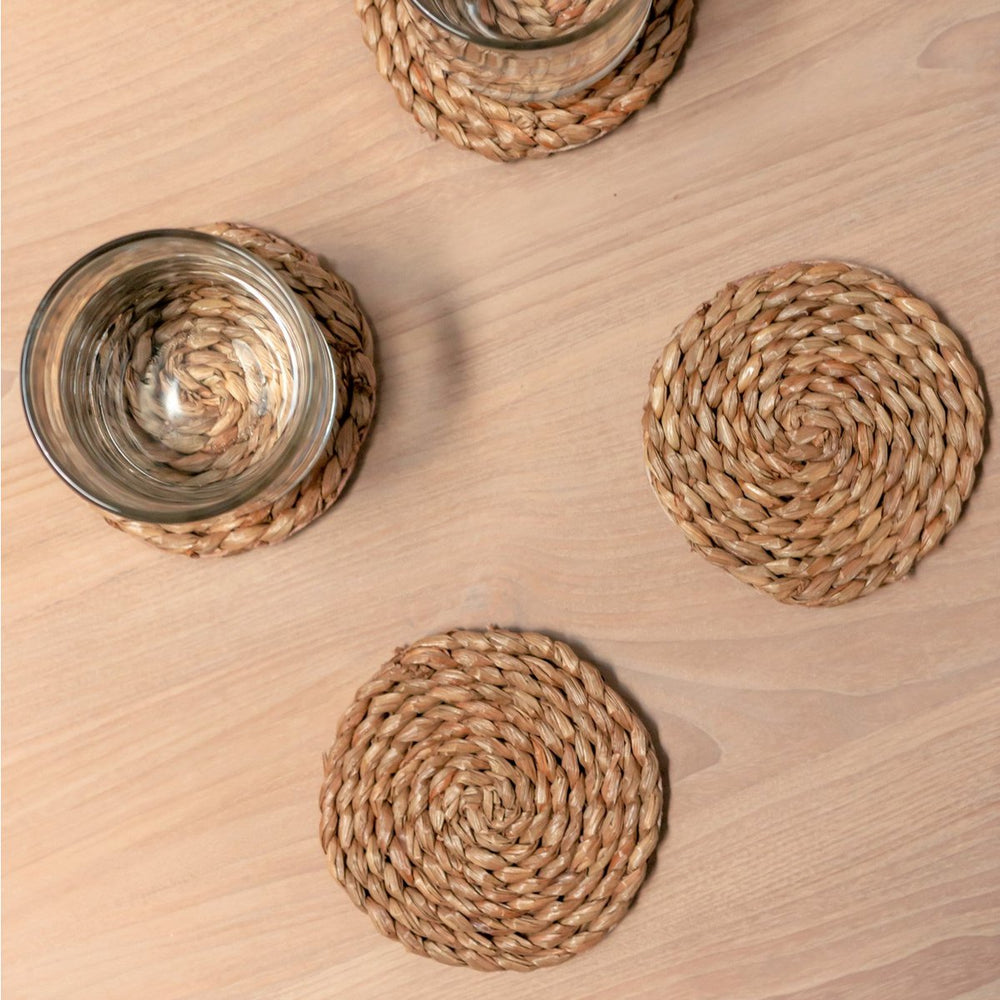 Round woven coasters on a wooden surface with glasses.