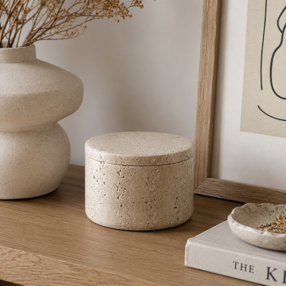 Decorative stone box on a wooden surface with a vase and framed art in the background.