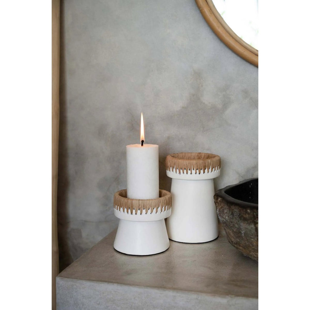 Two white candle holders with wooden accents on a surface, one holding a lit candle.