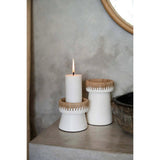 Two white candle holders with wooden accents on a surface, one holding a lit candle.