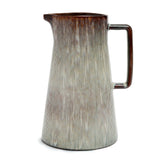 Ceramic pitcher with textured surface and brown handle on a white background