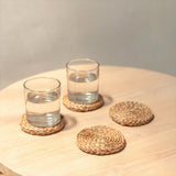 Two glasses of water on woven coasters on a wooden surface with a neutral background