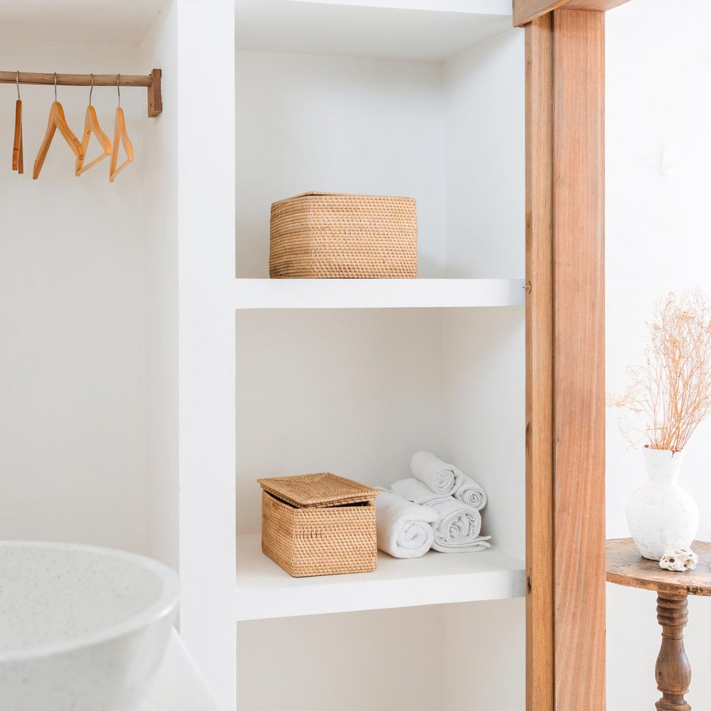 White shelving unit with woven baskets and rolled towels in a bathroom setting.