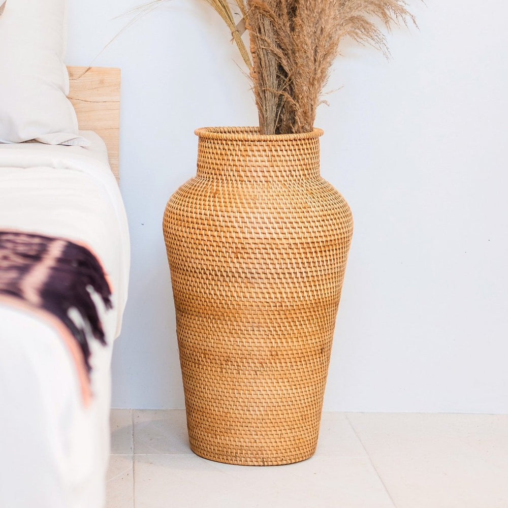 Woven rattan vase with dried plants on a white floor and wall background