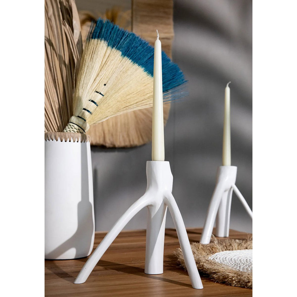 White candle holders with candles on a wooden surface, with decorative elements in the background.