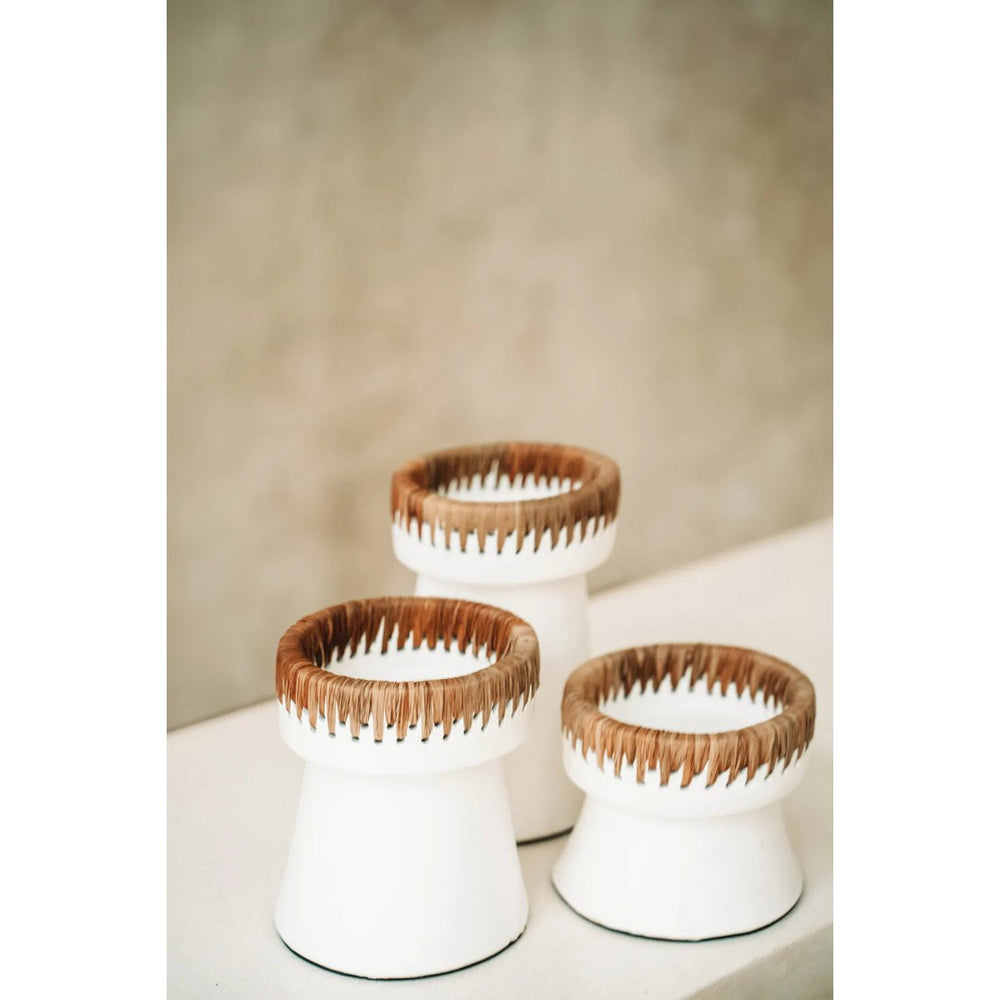Three white candle holders with brown wicker tops on a neutral background