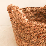 Close-up of a woven basket with a braided handle on a light background