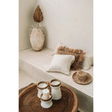 Decorative setting with candles, a vase, and pillows on a shelf.