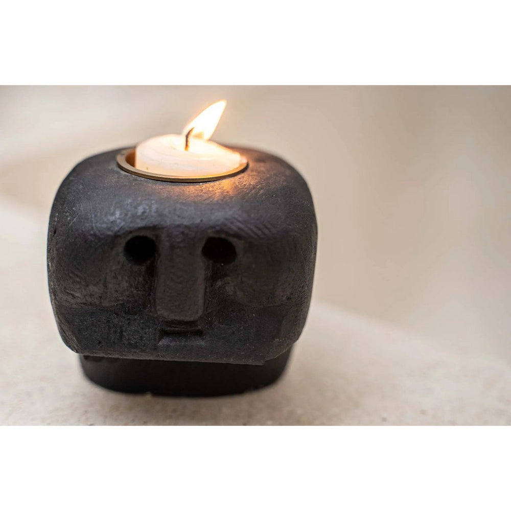 Candle holder shaped like a face with a lit candle inside on a neutral background